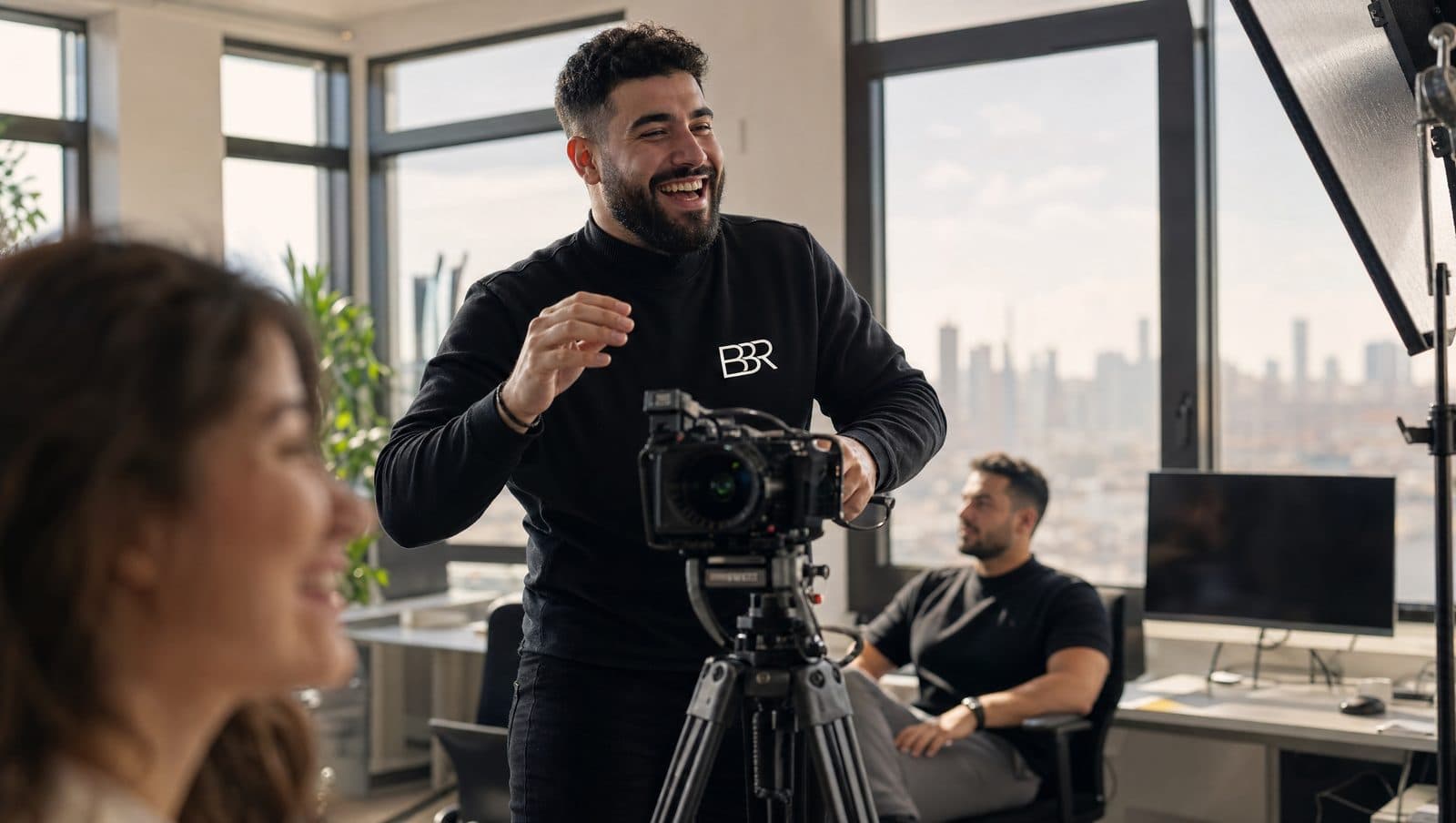 Burak Baris lacht hinter der Kamera bei einer Videoproduktion mit Stativ und Set-Licht