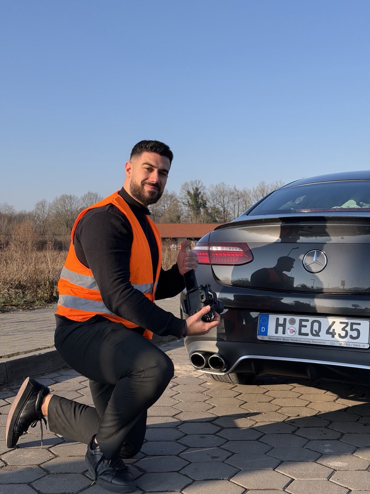 Burak Baris mit Kamera und Warnweste beim Content-Dreh an einem Mercedes in Hannover